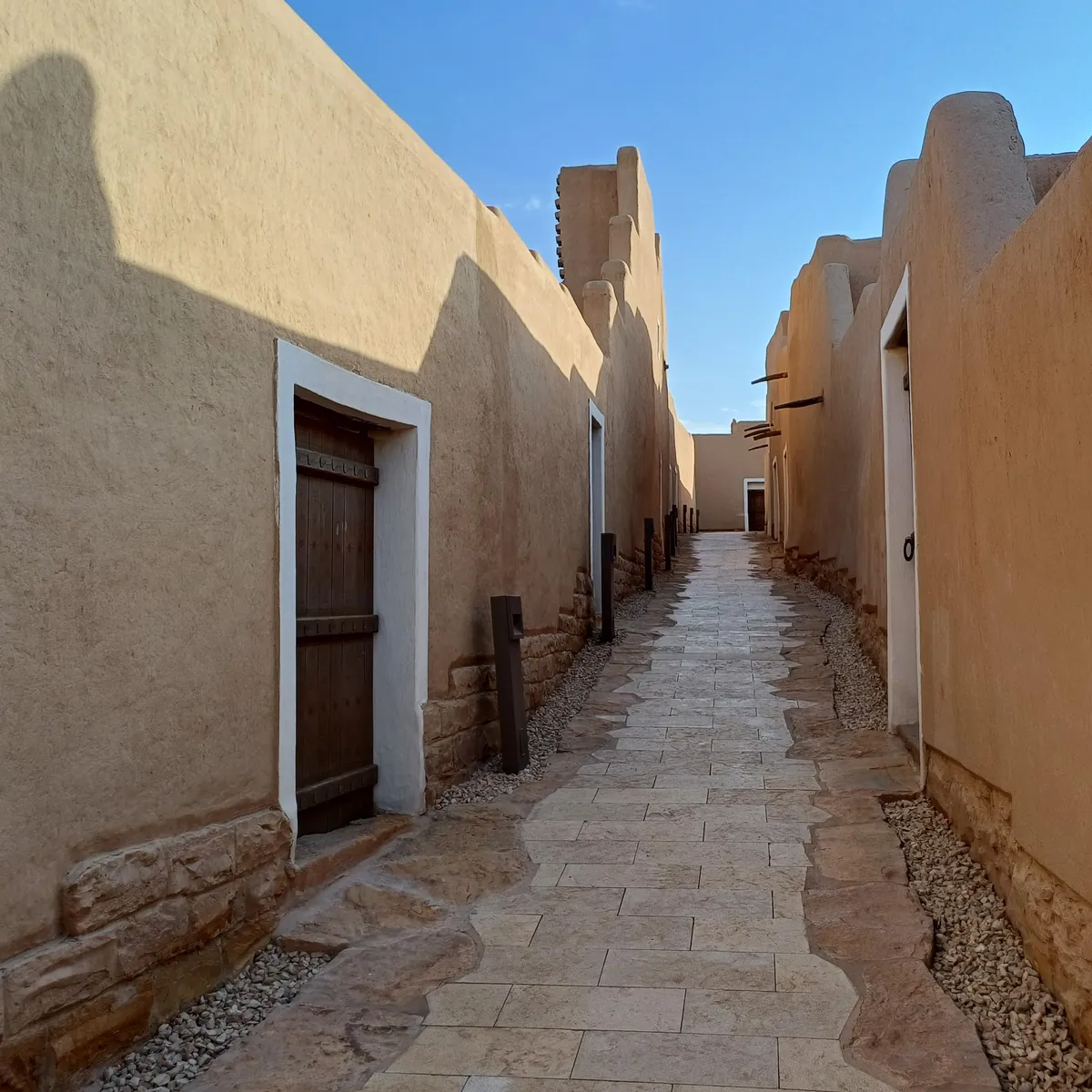 زقاق ضيق بين جدارين طينيين في حي الطريف، والضوء يسقط من أعلى الممر.